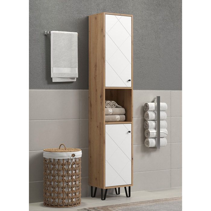 Hoge badkamerkast met twee witte deuren, open vak en zwarte pootjes naast een rieten wasmand in een badkamer