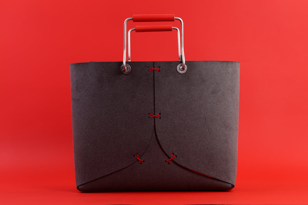 Grote grijze tas met rode stiksels en metalen handgrepen met rode grepen tegen een rode achtergrond